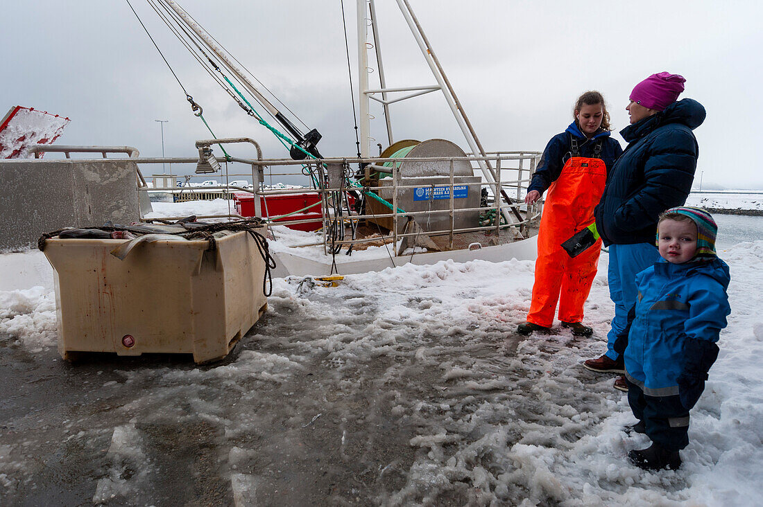 Eine Fischerfamilie wartet in einer Kabeljau verarbeitenden Fabrik im Hafen von Nordmela. Nordmela, Vesteralen-Inseln, Nordland, Norwegen.