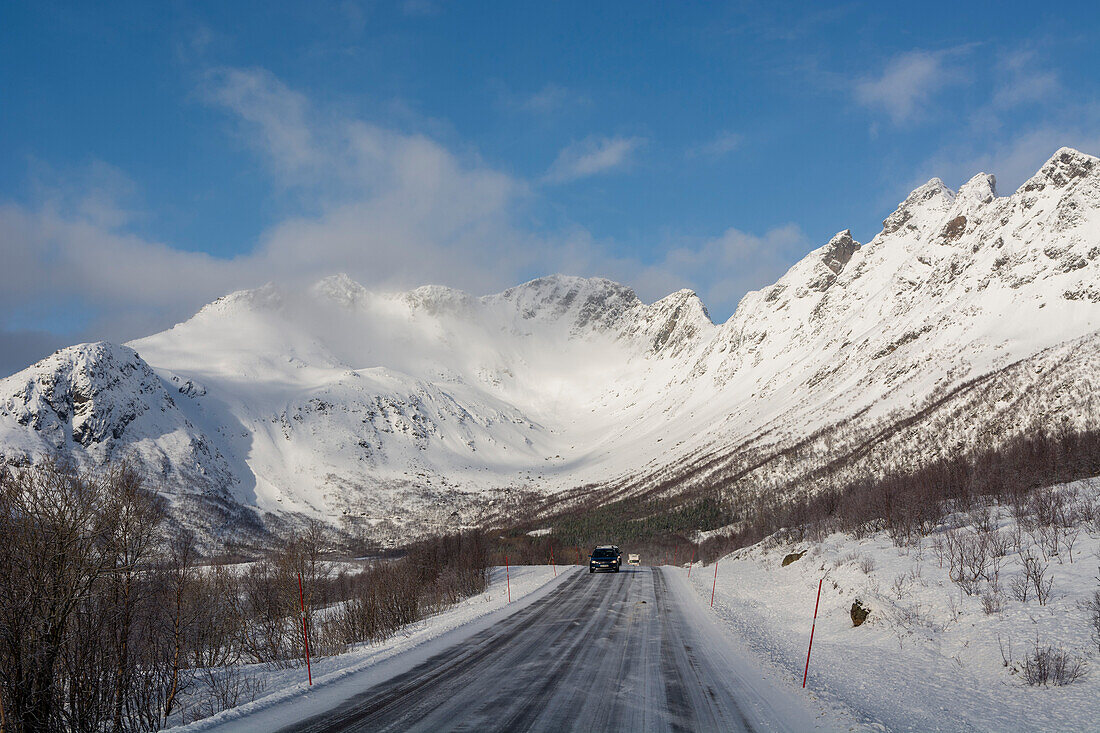 Cars driving on the National Tourist Road through a snowy mountain landscape. Svolvaer, Lofoten Islands, Nordland, Norway.