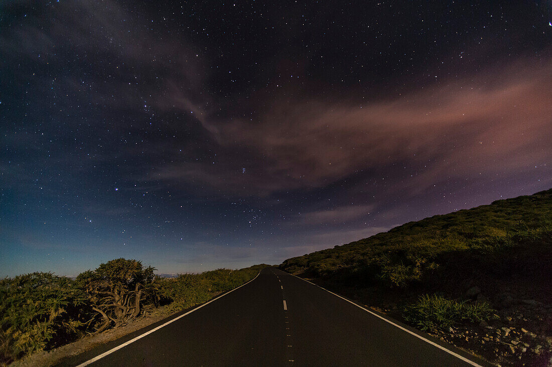 Eine Landstraße führt unter einem sternenübersäten Himmel zum Horizont. Insel La Palma, Kanarische Inseln, Spanien.
