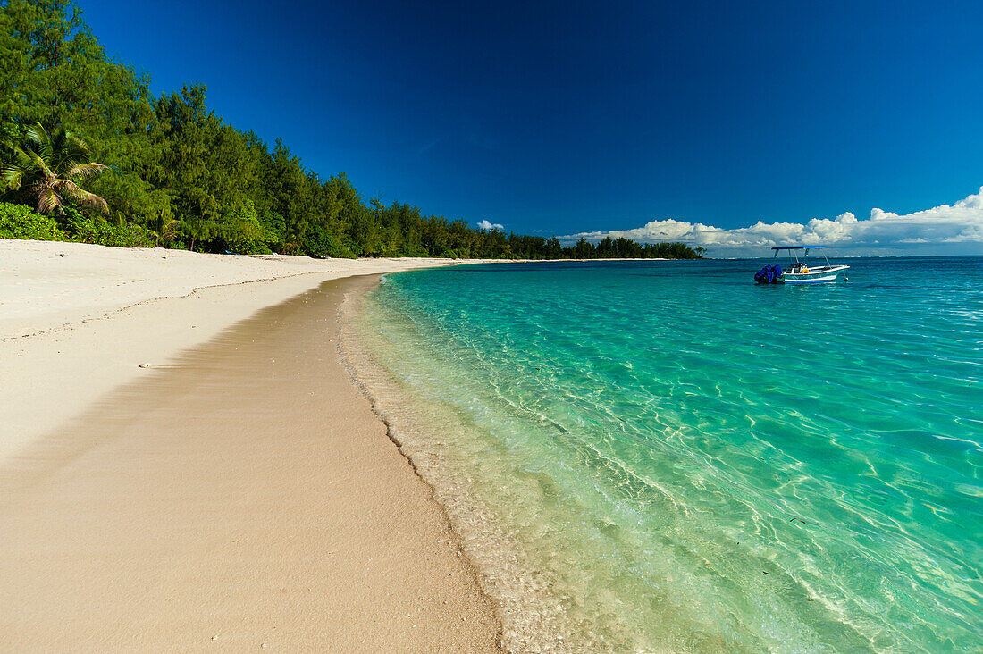 Ein Boot ankert vor der Küste eines unberührten tropischen Strandes. Denis-Insel, Republik Seychellen.