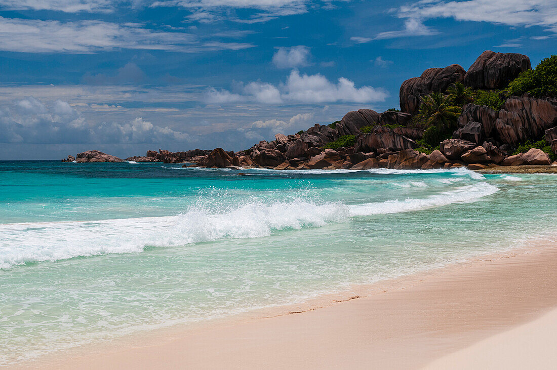 Large stone rock formations on a tropical beach with Indian Ocean surf. Grand Anse Beach, La Digue Island, The Republic of the Seychelles.