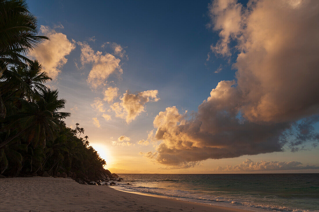 Sunset and puffy clouds over a palm-tree lined beach on the Indian Ocean. Anse Victorin Beach, Fregate Island, Republic of the Seychelles.