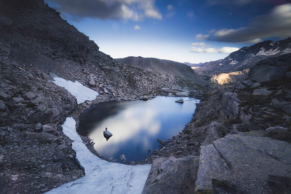 Man standing on a rock in the middle of a lake at Gran Paradiso National Park, Colle del Nivolet, Turin province, Piedmont, Italy