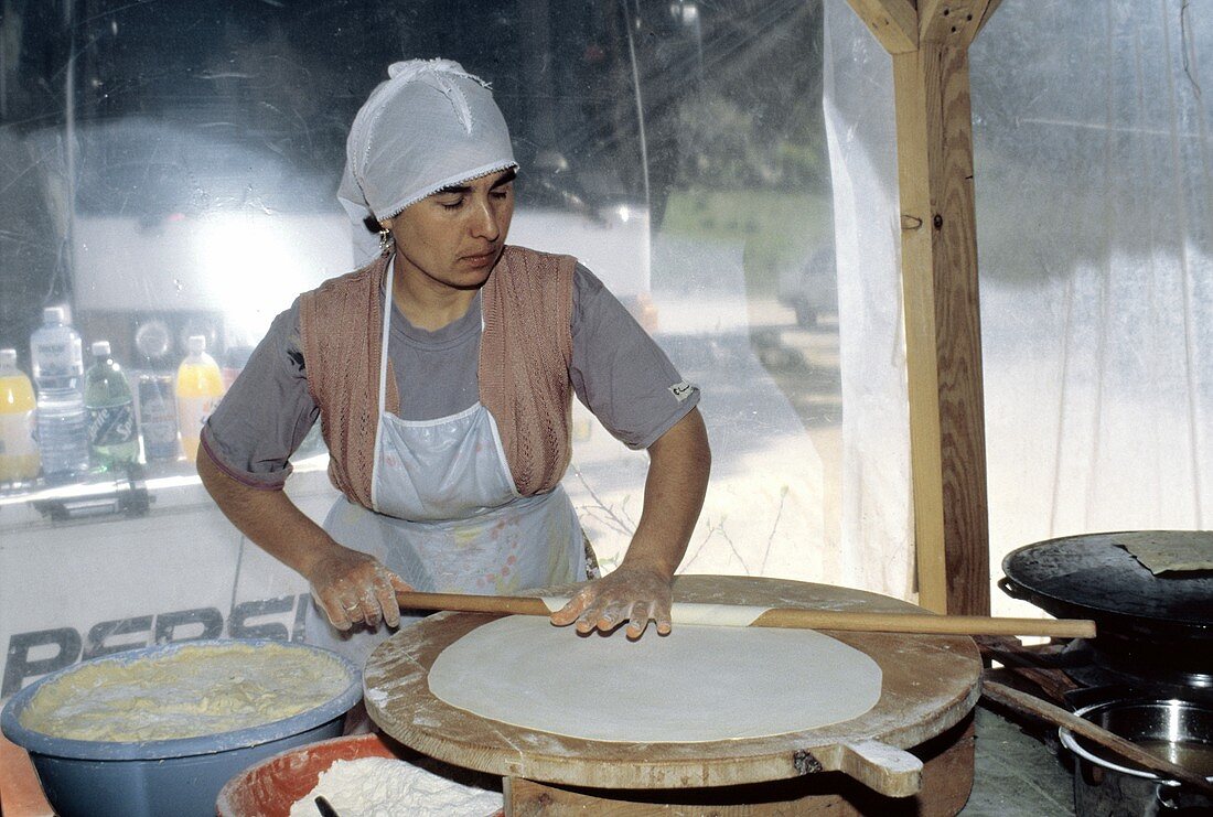 Türkische Frau beim Ausrollen von Teig für Fladenbrote