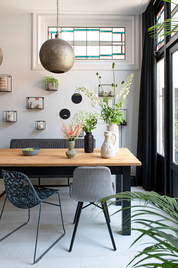 Dining area with various chairs, decorative objects on white wall and stained glass window