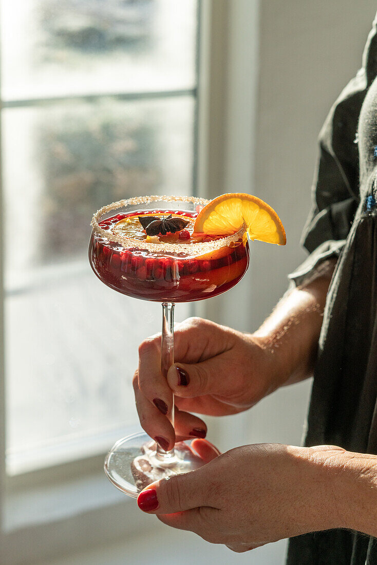 Frau hält Cocktailglas mit rotem Getränk und Orangenscheibe