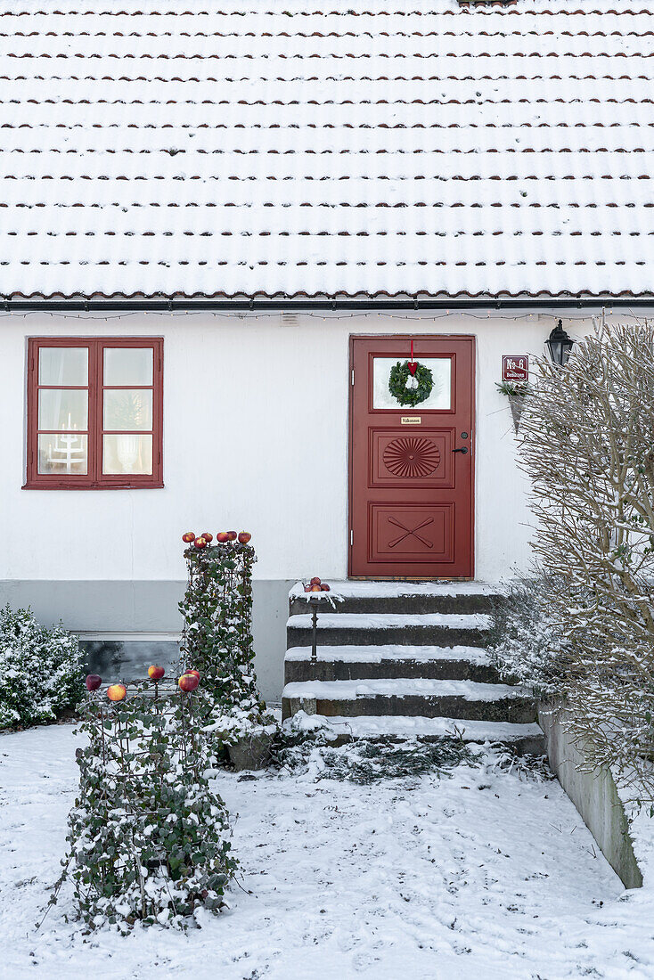 Entrance with red door and Christmas decorations in the snow