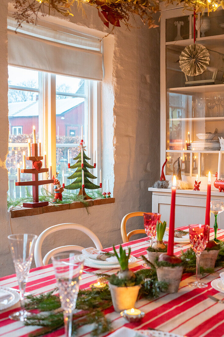 Weihnachtlich gedeckter Tisch mit roten Kerzen und Tannenbaum-Miniaturen auf dem Fensterbrett