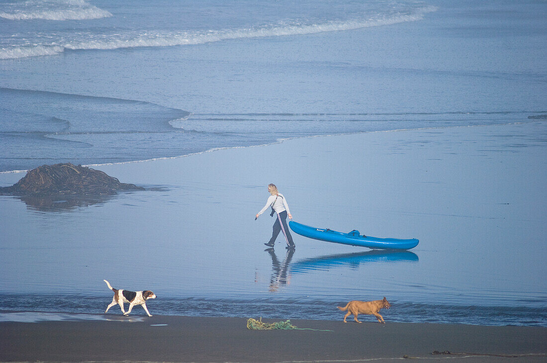 Frau beim Ziehen eines Kajaks am Strand von Myers Creek im Pistol River State Park an der Küste von Süd-Oregon.