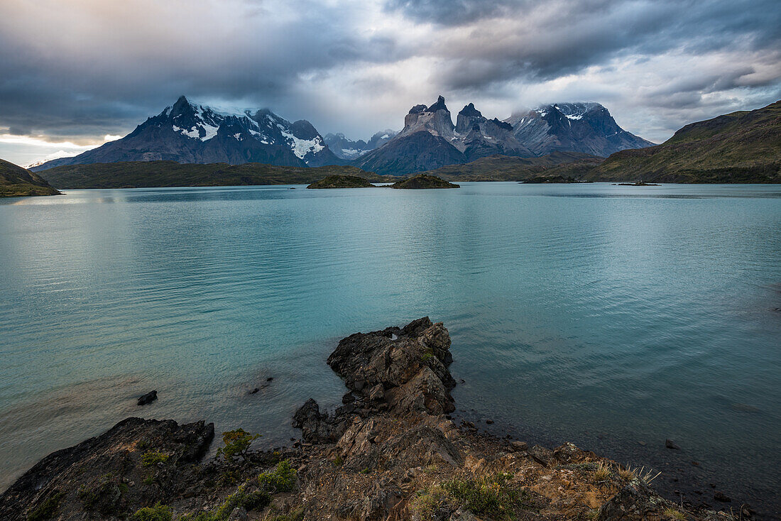 Das felsige Ufer des Lago Pehoe im Torres del Paine National Park, einem UNESCO-Biosphärenreservat in Chile in der Region Patagonien in Südamerika. Auf der anderen Seite des Sees liegt das Paine-Massiv in den tief hängenden Wolken.