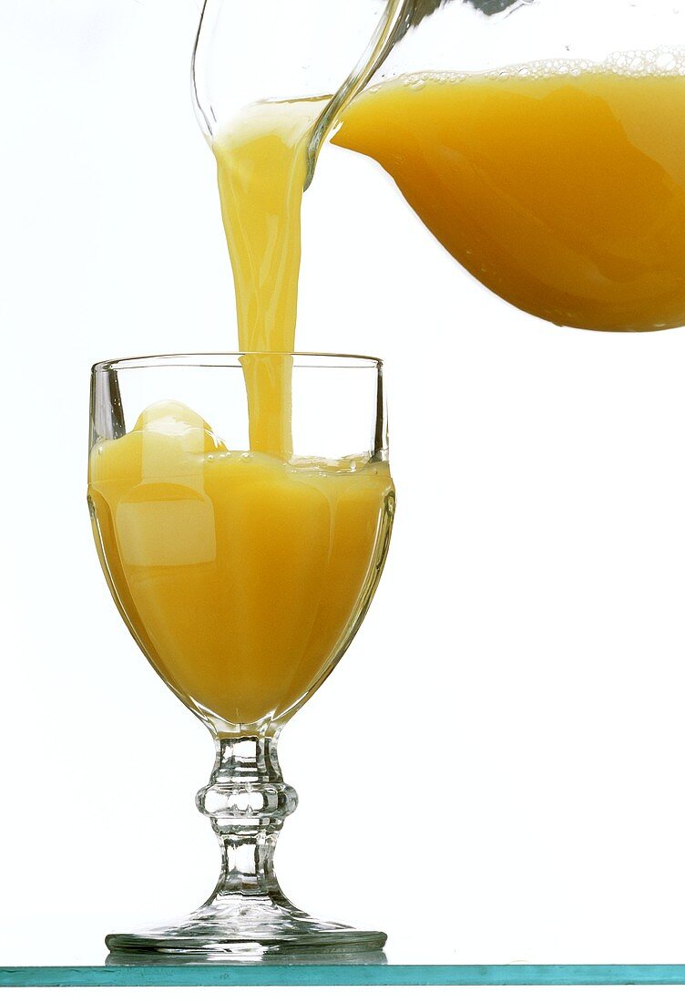 Orangensaft aus einem Glaskrug ins Saftglas gießen