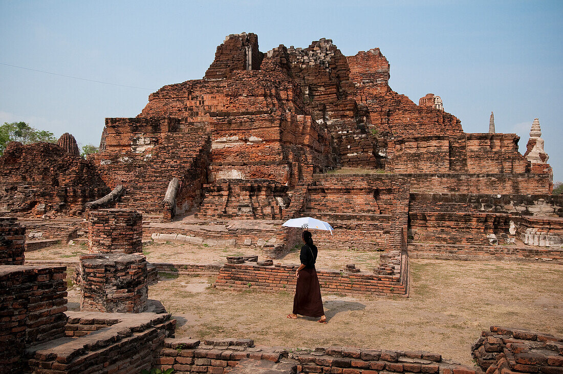 Besucherin mit Regenschirm in den Ruinen des buddhistischen Tempels Wat Mahathat, Ayutthaya, Thailand.