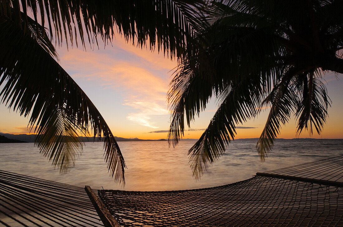 Hängematte und Palmen am Strand bei Sonnenuntergang, Matangi Private Island Resort, Fidschi.
