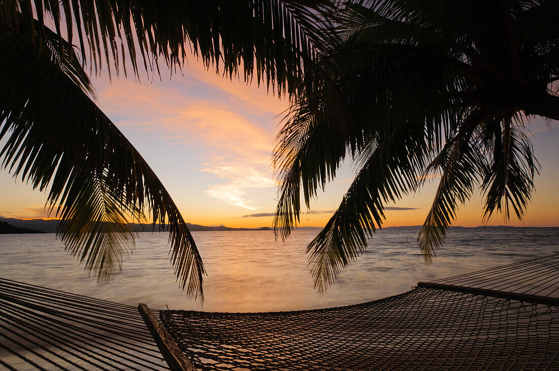 Hammock and palm trees on beach at sunset, Matangi Private Island Resort, Fiji.