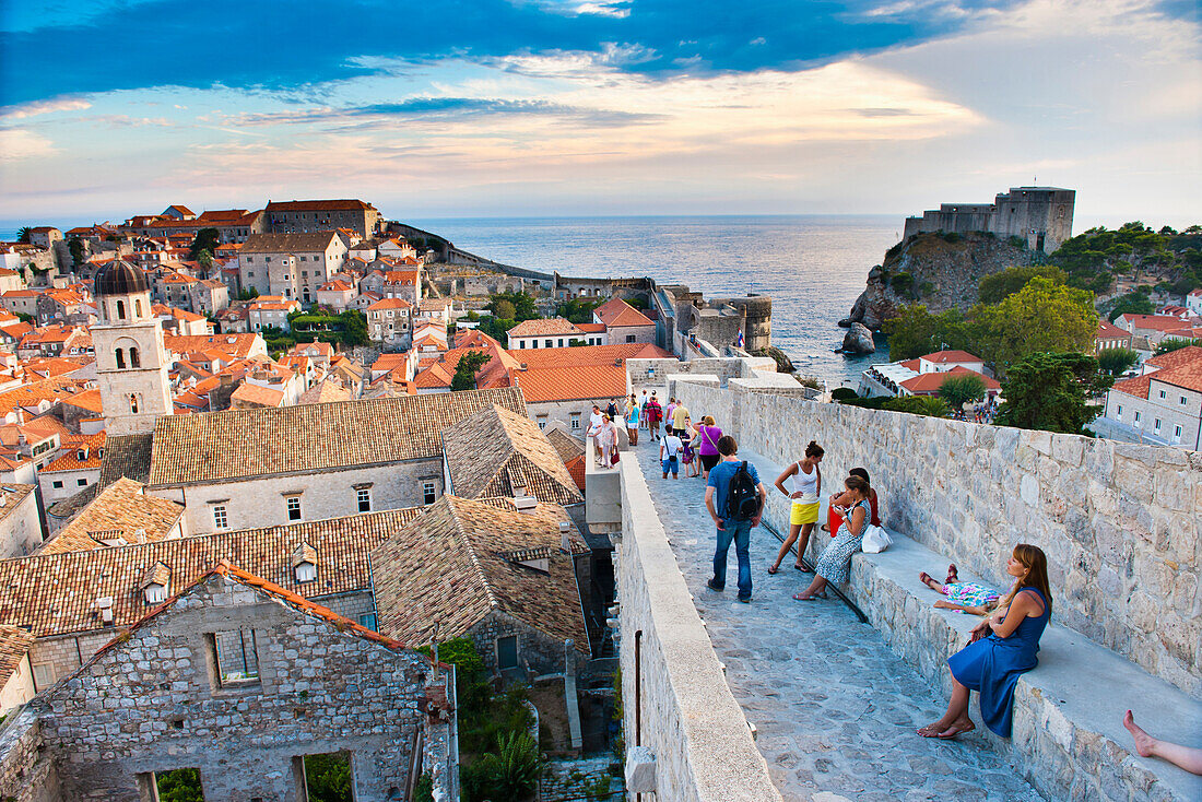 Foto von Touristen beim Besuch der Stadtmauern von Dubrovnik, Altstadt von Dubrovnik, Dalmatien, Kroatien. Dieses Foto zeigt einen Touristen, der die Stadtmauern von Dubrovnik besichtigt und die Aussicht auf die roten Ziegeldächer der zum UNESCO-Weltkulturerbe gehörenden Altstadt von Dubrovnik genießt. Für fast alle Touristen sind die Stadtmauern von Dubrovnik zweifellos der Höhepunkt eines Besuchs dieser schönen, historischen Altstadt an der dalmatinischen Küste Kroatiens. Die Stadtmauern von Dubrovnik bieten einen unvergleichlichen Blick auf das Franziskanerkloster, das Fort Lovrijenac und d