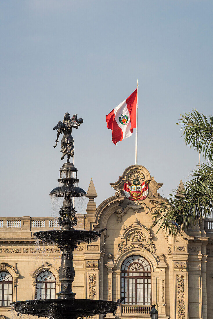 Die peruanische Flagge auf dem Regierungspalast und die bronzene Wasserfontäne auf der Plaza Mayor; Lima, Peru.