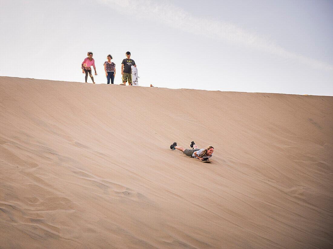 Sand boarding on dunes in the desert at Huacachina, Ica Region, Peru