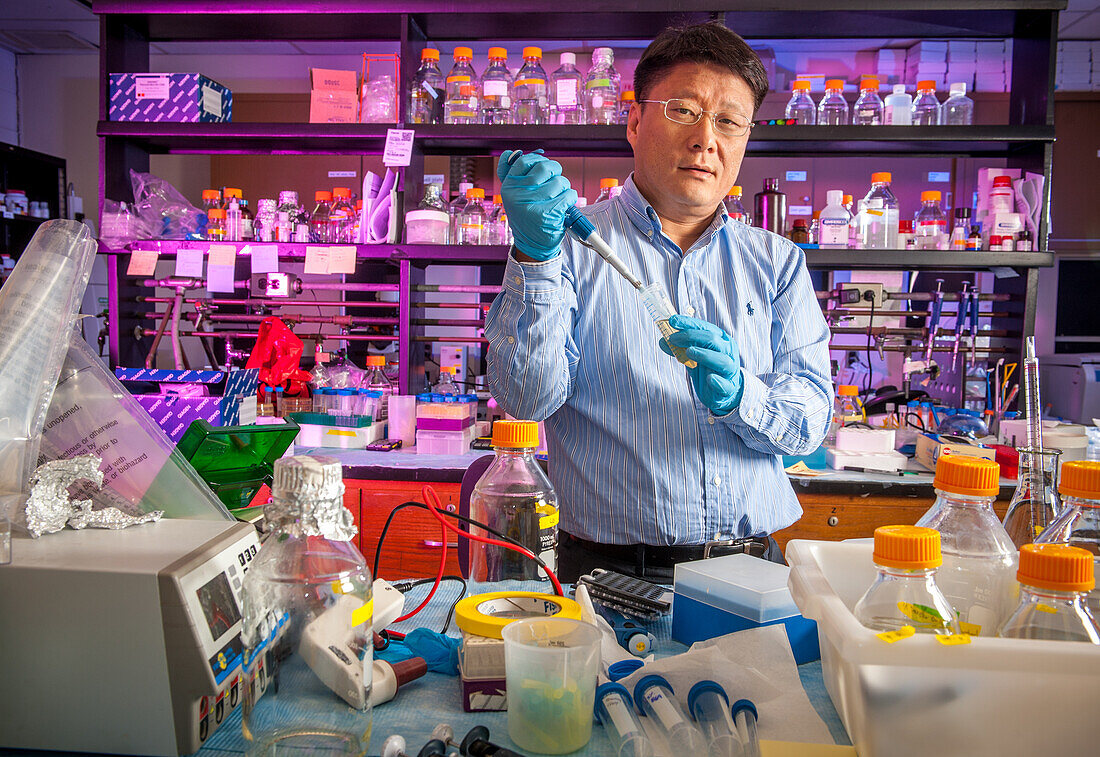 Male scientist in lab using pipette surrounded by lab equipment.