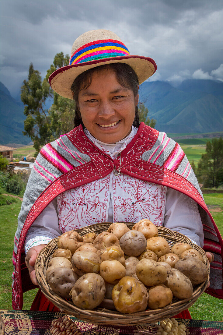Quechua-Frau, die einen Korb mit Kartoffeln hält und traditionelle Kleidung und Hut trägt, im Dorf Misminay, Sacred Valley, Peru.