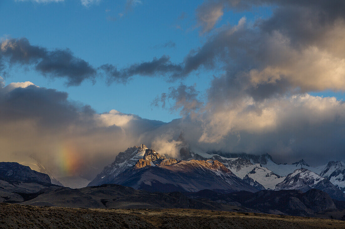 Clouds obscure the Fitz Roy Massif in Los Glaciares National Park near El Chalten, Argentina. A UNESCO World Heritage Site in the Patagonia region of South America. Visible are Loma de las Pizarras and Techado Negro, with a partial rainbow over the Torre Valley.