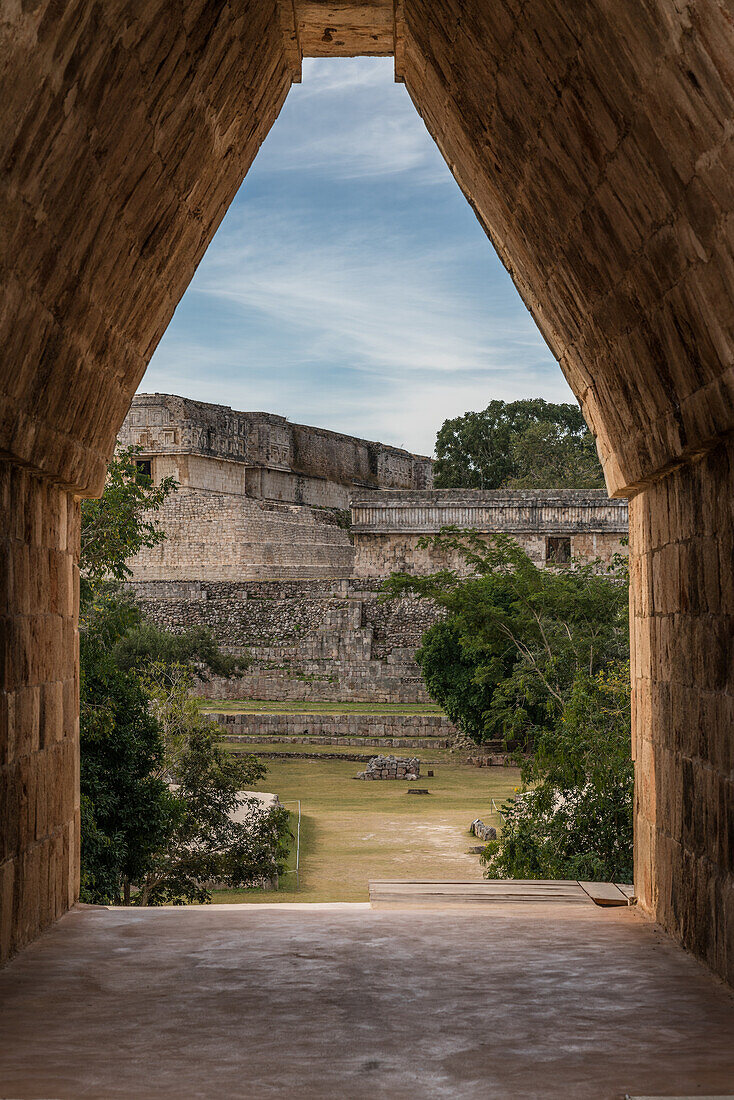 The main entrance into the Nunnery Quadrangle is through a corbel arch doorway in the center of the south building in the pre-Hispanic Mayan ruins of Uxmal, Mexico. This view is looking out at the Palace of the Governors and the House of the Turtles.
