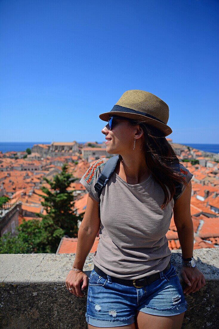 Junge erwachsene Frau mit Blick auf die Altstadt von Dubrovnik von der Stadtmauer aus, Kroatien