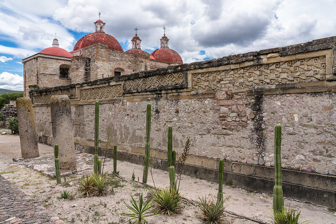 Two stone pillars in the ruins of the Zapotec city of Mitla. In the background is the Church of San Pablo. Mitla, Oaxaca, Mexico. A UNESCO World Heritage Site.