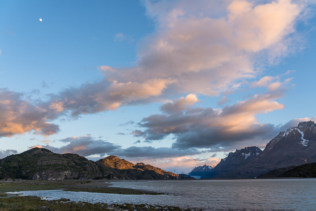 Der Mond und die bunten Wolken bei Sonnenaufgang über dem Lago Grey im Torres del Paine Nationalpark, einem UNESCO-Biosphärenreservat in Chile in der Region Patagonien in Südamerika.