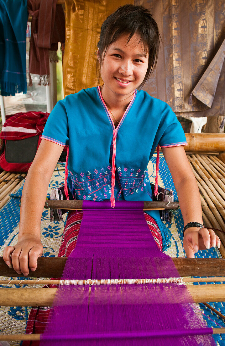 Young woman weaving cloth on loom; Patara Elephant Farm, Chiang Mai Province, Thailand.