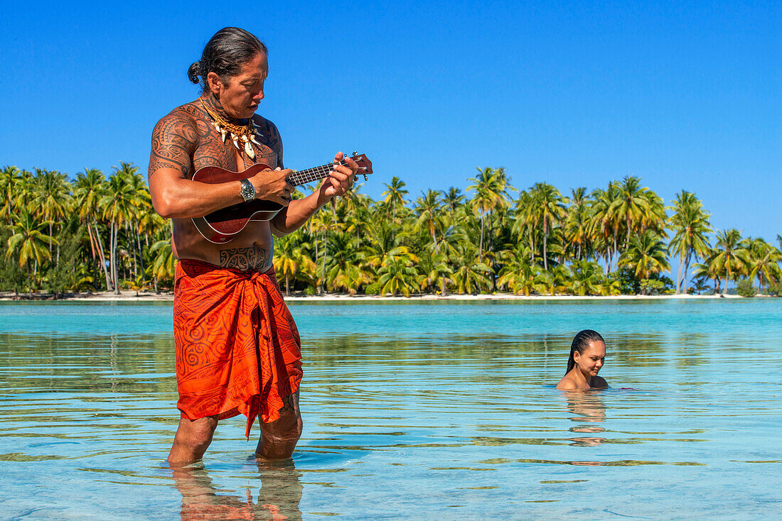 Insel Taha'a, Französisch-Polynesien. Ein einheimischer Junge spielt auf der Ukulele, um ein Mädchen auf dem Motu Mahana zu umwerben, Taha'a, Gesellschaftsinseln, Französisch-Polynesien, Südpazifik.