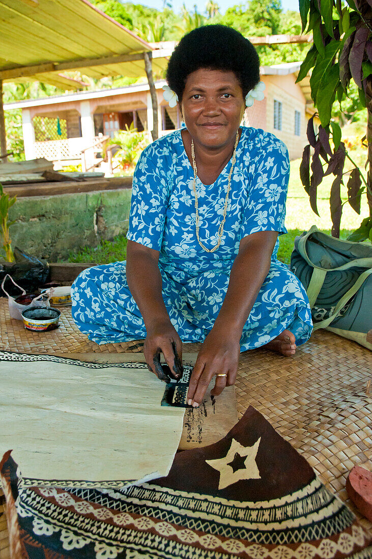Fidschianerin malt ein Muster auf Tapa-Stoff; Dorf Tongo, Insel Qamea, Fidschi.