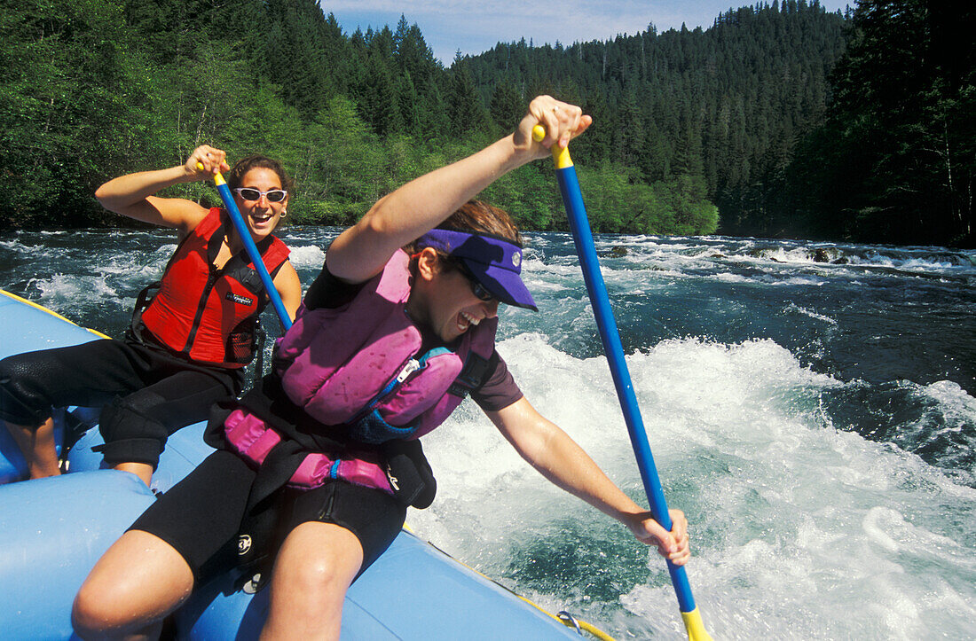 Two young women paddling inflatable raft through whitewater on the North Umpqua River; Cascade Mountains, Oregon.