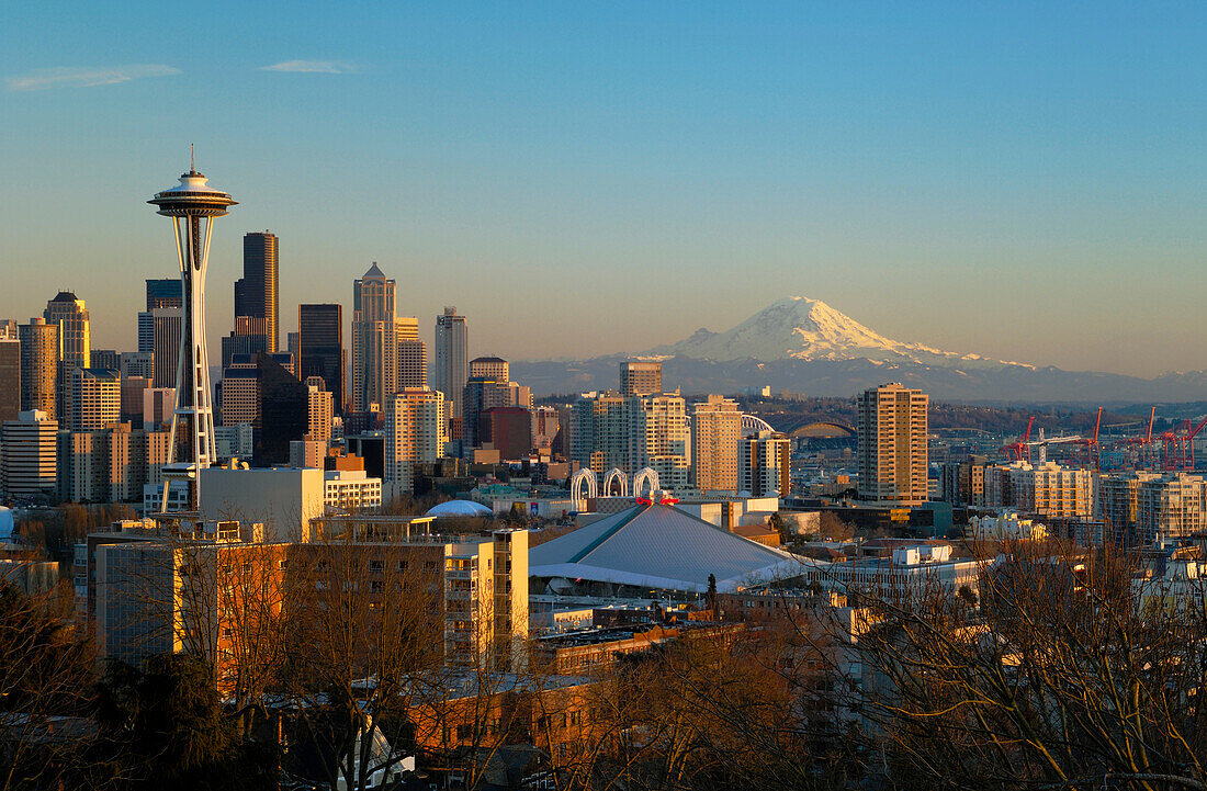 Skyline der Stadt bei Sonnenuntergang mit der Space Needle, dem Stadtzentrum und dem Mount Rainier vom Queen Anne Hill aus; Seattle, Washington.