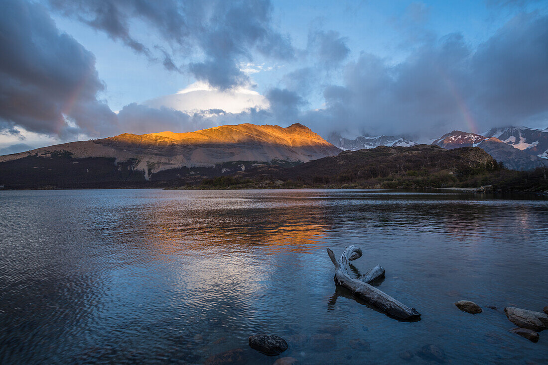 Sunrise lights up the Loma de las Pizarras by Lago Capri in Los Glaciares National Park near El Chalten, Argentina. A UNESCO World Heritage Site in the Patagonia region of South America. The Fitz Roy Massif is hidden by the clouds at right, behind the rainbow.