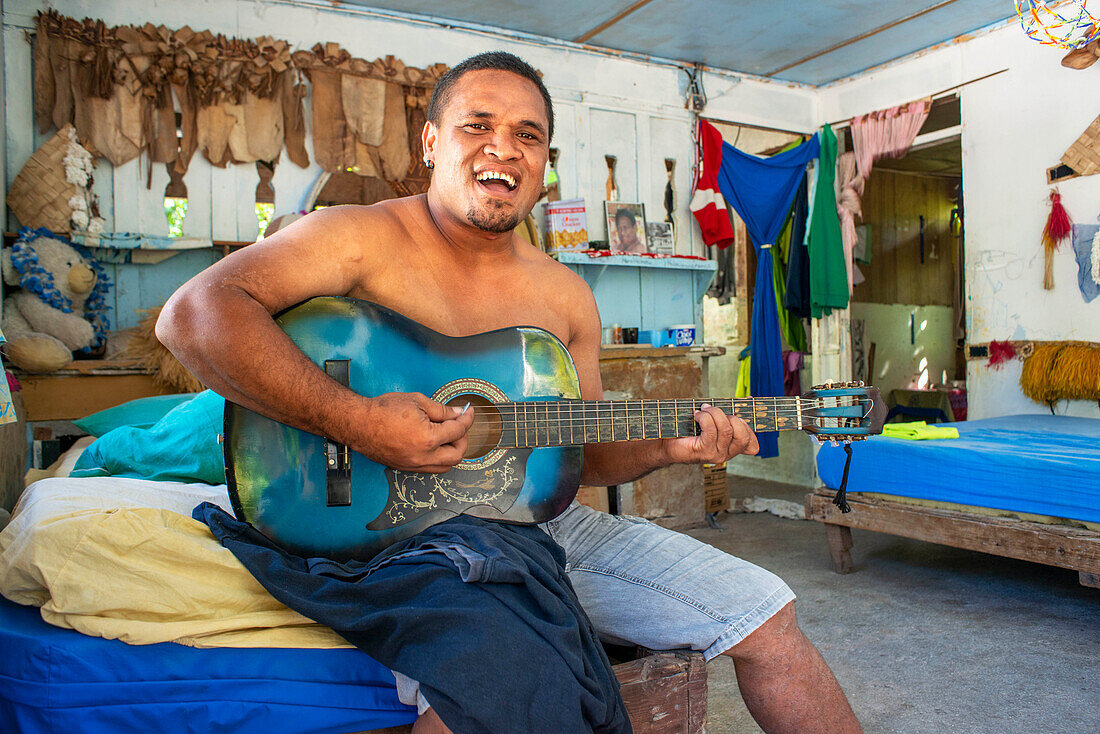 Innenansicht eines traditionellen Hauses in Rangiroa, Tuamotus-Inseln, Französisch-Polynesien, Südpazifik. Ein Mann spielt Gitarre und singt mit seiner Familie.