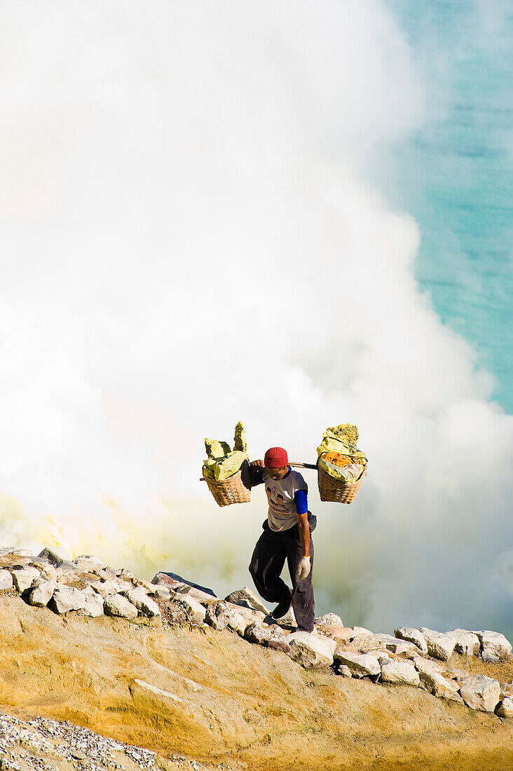 Schwefelarbeiter am Kawah Ijen, Java, Indonesien. Kawah Ijen ist ein Vulkan mit einem aktiven Krater und einem Säuresee in Ost-Java, Indonesien. Er ist ein unglaubliches und unverzichtbares Ziel für jeden, der Java oder Bali besucht. Nicht nur die Aussicht auf der 4 km langen Wanderung zum Kraterrand ist beeindruckend, sondern auch das, was sich dort abspielt, ist atemberaubend. Auf dem Weg zum Boden des Kwah Ijen (Ijen-Krater) bauen Hunderte von indonesischen Männern, viele in Flipflops, Schwefel aus dem Herzen des Vulkans ab. Sie beladen ihre Körbe mit bis zu 80 kg Schwefel, bevor sie sich a