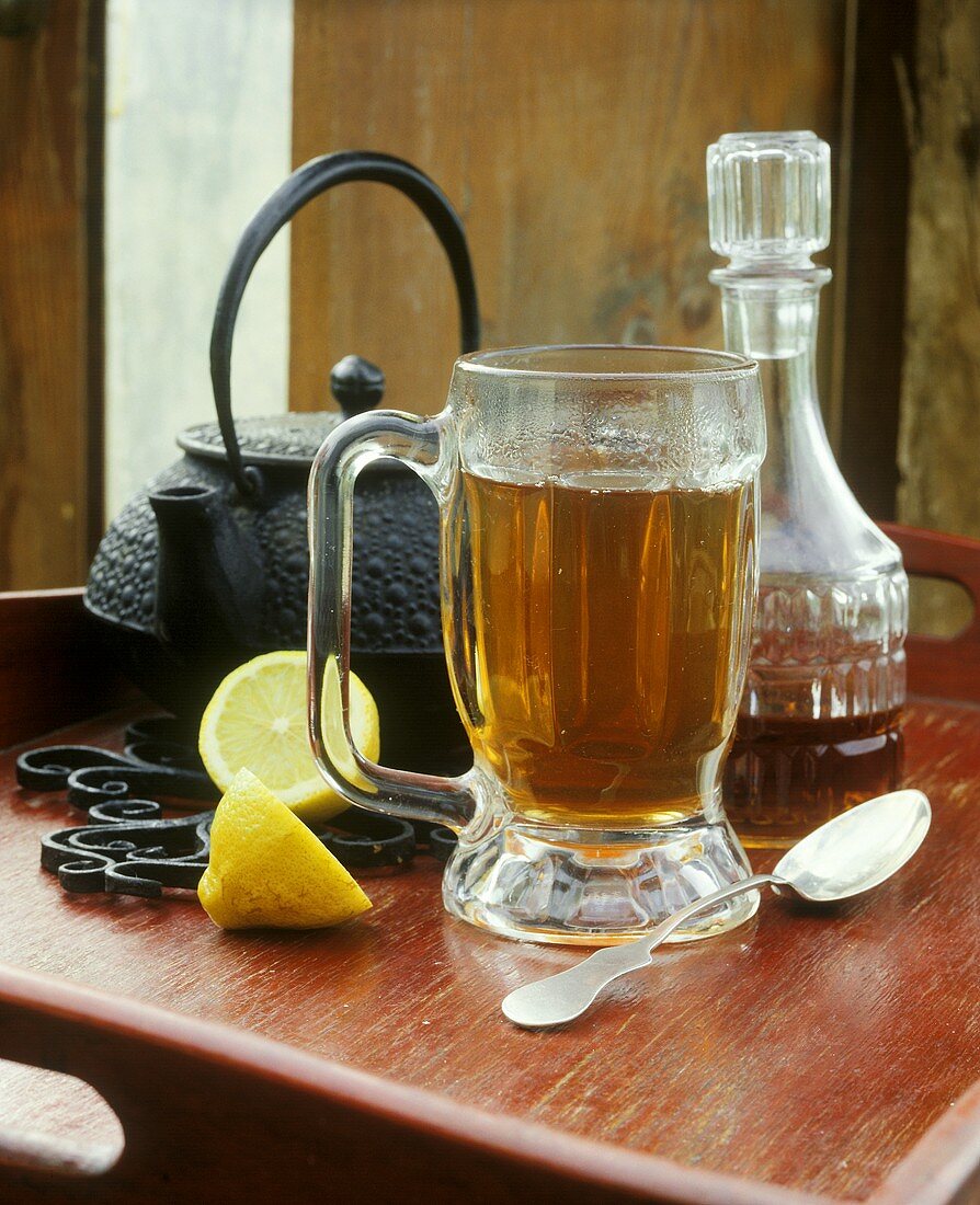 Punch in tall glass, teapot, lemon and carafe of rum
