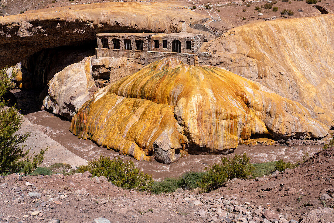 Farbenfrohe Travertinablagerungen der Mineralquelle in Puente del Inca in den argentinischen Anden mit den Ruinen eines ehemaligen Kurortes.