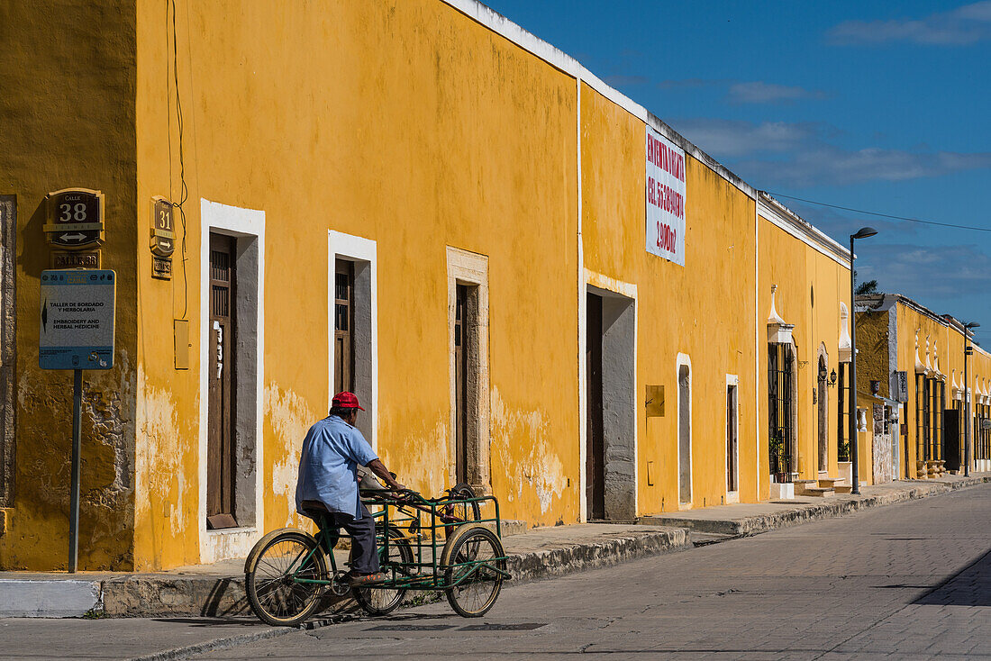 Ein Mann fährt auf seinem Lastendreirad auf der Straße in Izamal, Yucatan, Mexiko, bekannt als die Gelbe Stadt. Die historische Stadt Izamal gehört zum UNESCO-Weltkulturerbe.