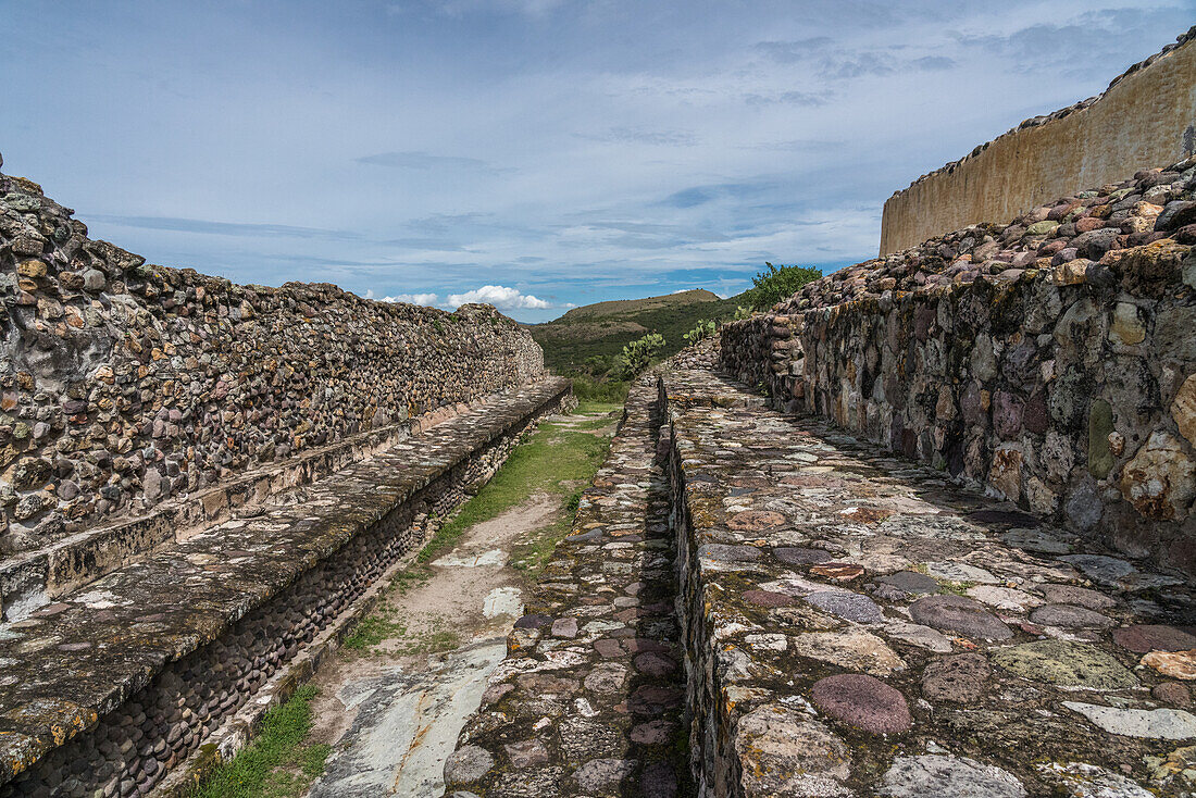 Die verzierte Straße trägt ihren Namen wegen einiger Bereiche mit Laubsägearbeiten in Bodennähe auf der Rückseite der Ratshalle (links). Rechts ist das Fundament des Palastes der 6 Patios zu sehen. Yagul, Oaxaca, Mexiko.
