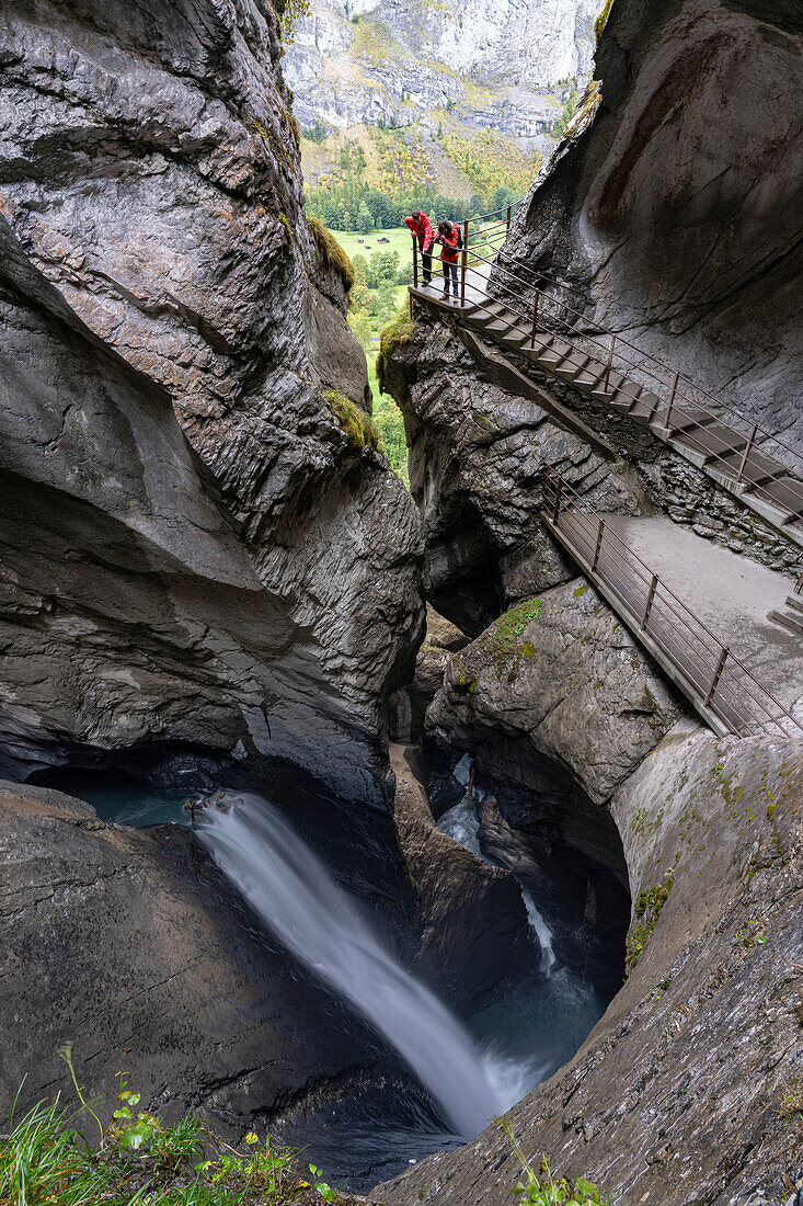 Zwei Wanderer fotografieren die Trummelbachfälle von einem Pfad in einer majestätischen Felsschlucht, Lauterbrunnen, Kanton Bern, Schweiz, Europa