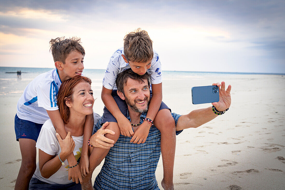 Glückliche Familie mit zwei Jungen, die ein Selfie mit Smartphone am Strand machen, Sansibar, Tansania, Ostafrika, Afrika