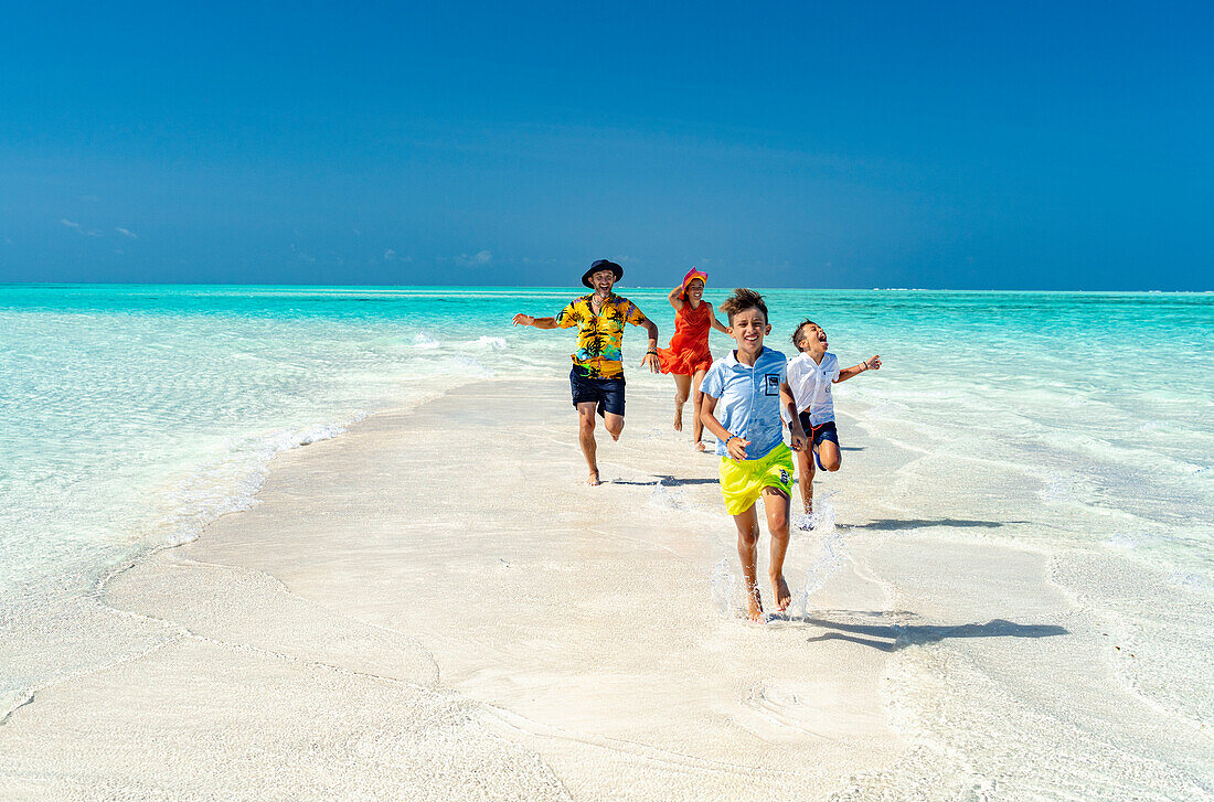 Fröhliche Eltern mit Söhnen, die an einem idyllischen, leeren Strand rennen, Sansibar, Tansania, Ostafrika, Afrika