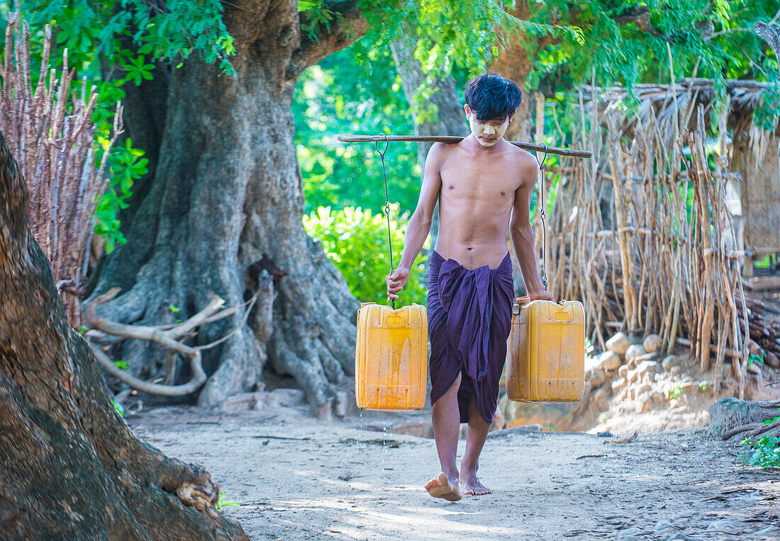 Ein burmesischer Bauer trägt mit Wasser gefüllte Plastikeimer in einem Dorf bei Bagan