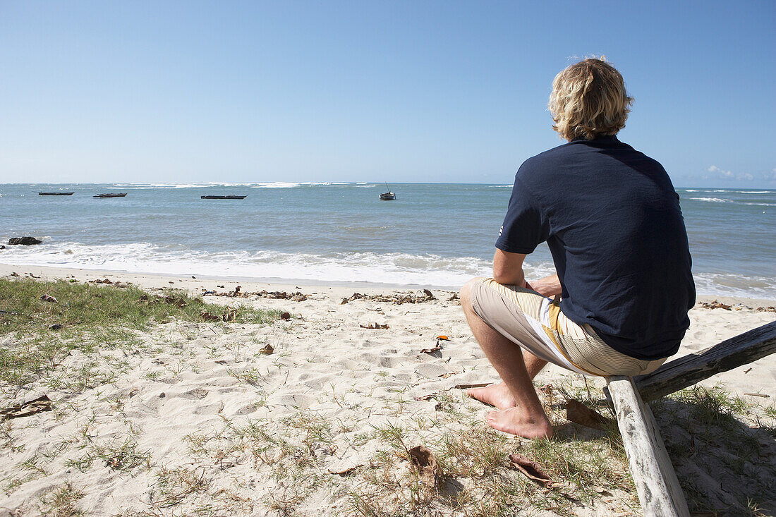 Mann sitzt am Strand und schaut auf das Meer hinaus