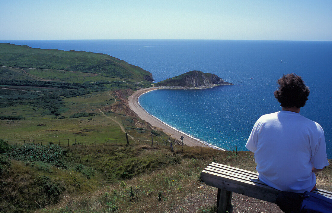 Frau sitzt auf einer Bank an der Küste, hoher Blickwinkel