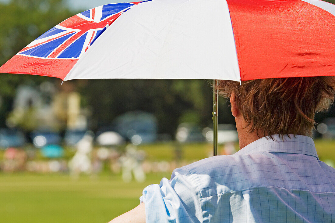 Rückansicht eines Zuschauers mit Regenschirm, der ein Kricketspiel an einem heißen Sommertag in Hastings verfolgt.