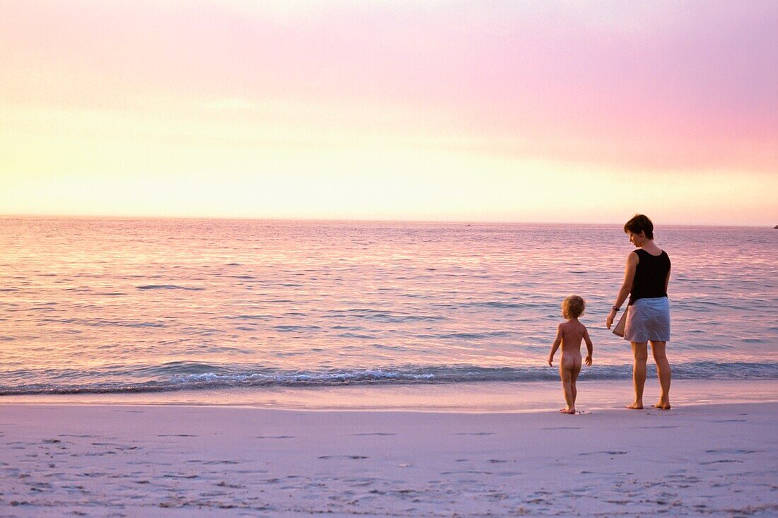 Mother And Son (2-3 Years) Standing On Beach At Sunset, Rear View