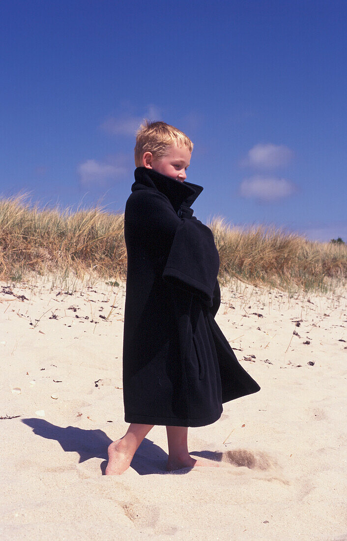 Junge am Strand in Mantel eingewickelt