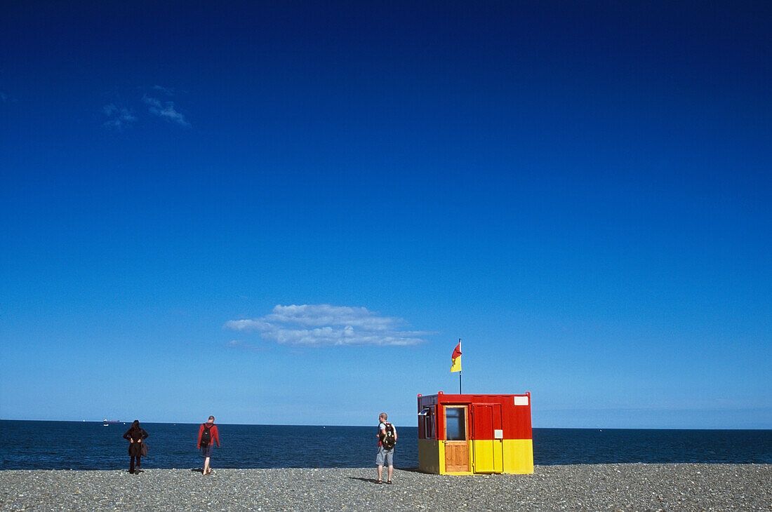 Drei Personen in der Nähe der Rettungsstation am Strand, Rückansicht